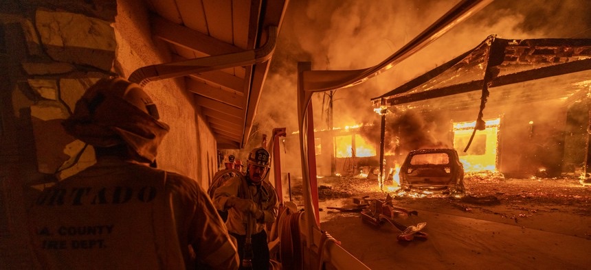Firefighters looking at a burning building with a car inside
